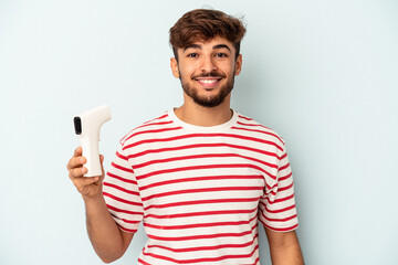 Young mixed race man holding thermometer isolated on blue background happy, smiling and cheerful.