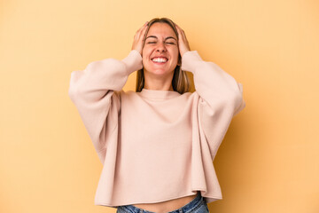 Young caucasian woman isolated on yellow background laughs joyfully keeping hands on head. Happiness concept.