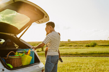 Young father holding his son while standing by car trunk outdoors