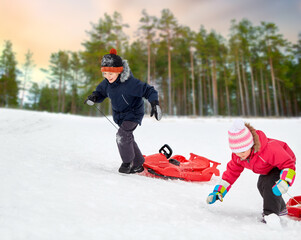 Fototapeta na wymiar childhood, sledging and season concept - happy little kids with sleds climbing snow hill in winter over pine forest on background