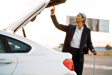 Grey asian woman opening trunk while standing with suitcase