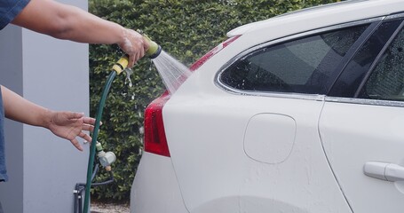 Asian man spray clean water to wash clean dirt foam on white car at home	
