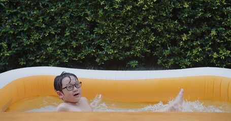 happiness cute Asian preschool little child boy wearing eyeglasses enjoy having fun swimming floating in small pool with splashing water, activity leisure in the summer day	
