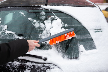 Winter problems with the car. A man cleans the car from snow with a brush