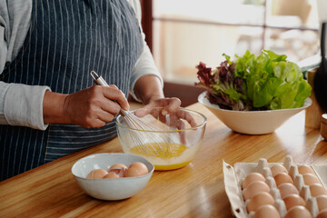 Close up of hands, elderly multi-cultural female whisking eggs for breakfast. Retired, healthy...