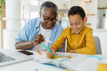 Grandfather tutoring his grandson at home. The child is patiently listening and learning while...