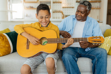 African America grandfather sitting at home with his grandson. Boy playing the guitar and singing.  - 474695182