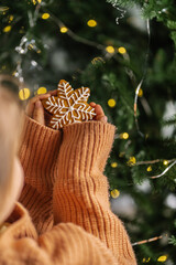 Ginger Christmas cookies in children's hands on the background of the Christmas tree.