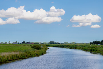 Fototapeta na wymiar Summer countryside landscape, Flat and low land with green meadow under blue sky, Typical Dutch polder with small river, canal or ditch, Small villages in Groningen, A city in the northern Netherlands