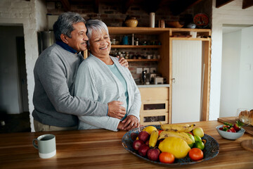 Happily retired elderly biracial couple standing, hugging. Healthy lifestyle in modern kitchen.