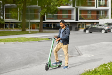 transport, technology and people and concept - happy smiling young man with electric scooter using smartphone on city street