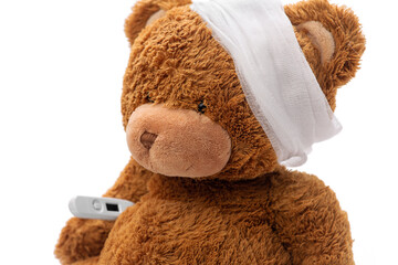 medicine, healthcare and childhood concept - teddy bear toy with bandaged head and thermometer on...