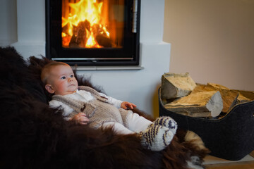cute little newborn baby in traditional outfit on a sheepskin seesaw infront of a chimney fireplace...