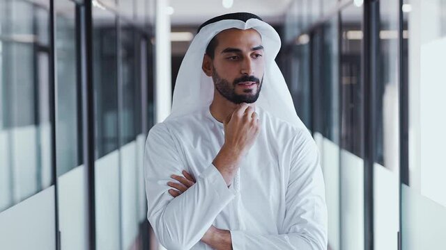 handsome man with dish dasha working in his business office of Dubai. Portraits of a successful businessman in traditional emirates white dress. Concept about middle eastern cultures