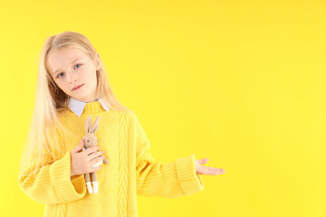 Cute little girl holds toy rabbit on yellow background