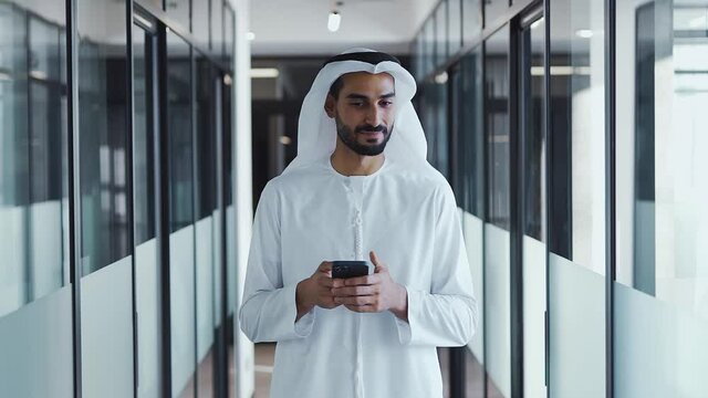 handsome man with dish dasha working in his business office of Dubai. Portraits of a successful businessman in traditional emirates white dress. Concept about middle eastern cultures