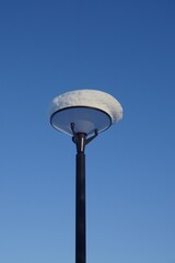 One ssolated street lamp with thick layer of snow on the top against blue clear sky. Winter season, close up view. Reidi tee street, Tallinn, Estonia. December 2021