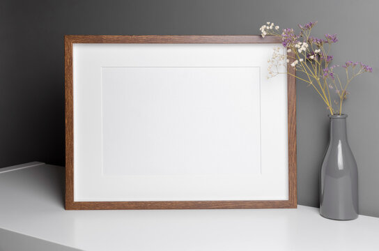 Landscape wooden frame mockup for artwork, photo and print presentation with dry flowers over grey wall.