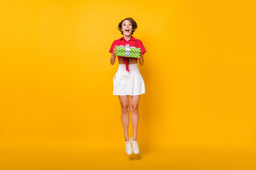 Full size photo of impressed nice brunette lady jump with present wear shirt skirt isolated on yellow background