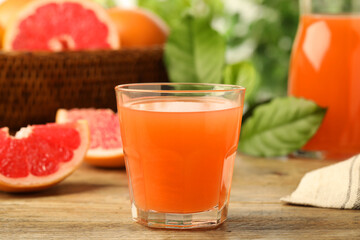 Glass of delicious grapefruit juice on wooden table against blurred background