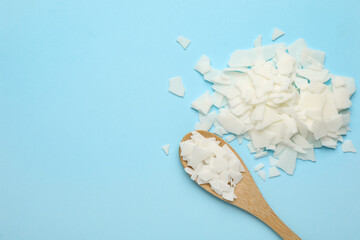 Wooden spoon and soy wax flakes on light blue background, flat lay with space for text. Homemade candle material