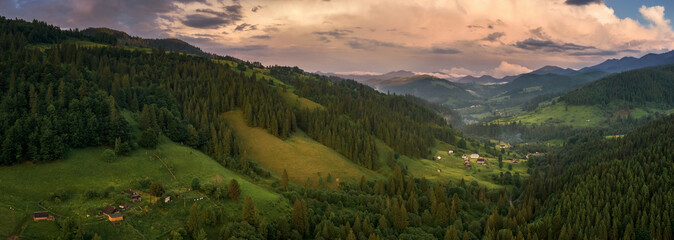 Panorama of Ukraine mountain countryside with dramatic colorful cloudy sky before the rain. Scenic hilly landscape of remote mountain village in Ukrainian Carpathians
