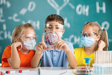 Focused kid pouring liquid into flask while conducting experiment with colorful reagents