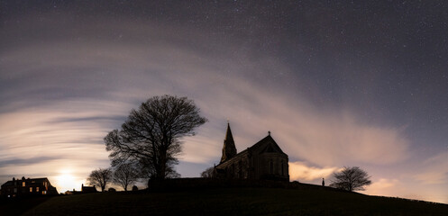 A church in moonlight on top of a hill under a blanket of stars