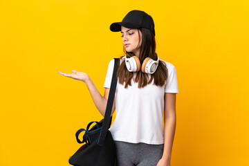 Young sport woman with sport bag isolated on yellow background holding copyspace with doubts