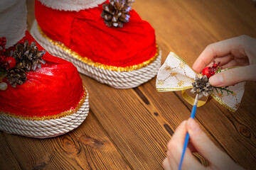 The girl's hands make a bow for santa claus boots. Handmade decorations for Christmas and New Years. Wood background, close-up