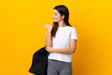 Young sport woman with sport bag isolated on yellow background pointing to the side to present a product