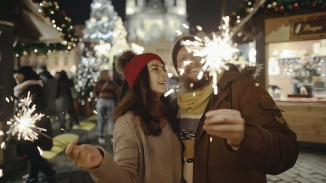 Romantic couple in love hugging and burning the sparklers at festive street fair. Lovers travelling to Europe at the height of Christmas holidays. Sweethearts kissing in the centre of old city.
