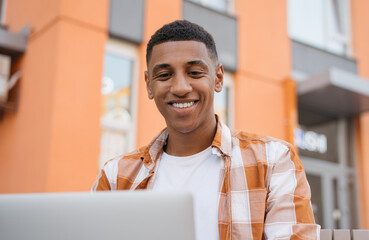 Young smiling African American student studying sitting in university campus, education concept. Handsome businessman using laptop computer, working online planning start up. Successful business