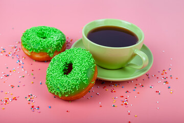 Green donuts and a cup of coffee on a pink background.