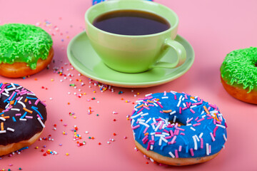 Multicolored donuts and a cup of coffee on a pink background.