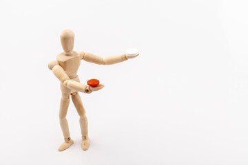 A wooden Gestalta doll or mannequin holds red and white pills in its hands on light background. The concept of choice.