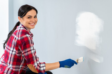 Indoor view of the brunette woman looking at the camera while painting with special brush repair equipment her walls at the room and feeling satisfied