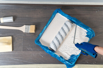 Cropped view of the caucasian woman holding paint roller at her hands while picks up paint from a container and enjoying renovation time at home. Repair and remodeling concept