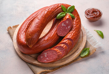 Smoked, Krakow sausage on a cutting board with basil and sauce.