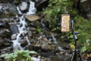 Taking video of mountain stream with modern phone on tripod outdoors