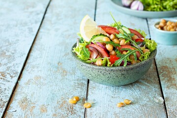 Healthy Vegetarian Chickpea Salad in a bowl with vegetables, herbs and dressing on a blue wooden background. Healthy food concept.