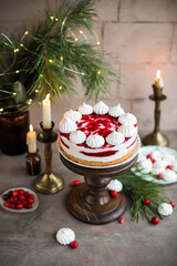Sponge mousse cake with cranberry jam and decorated with meringues. Festive cake for the New Year's table with candles and pine branches.
