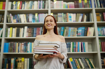 Woman holding stack of books near bookshelves