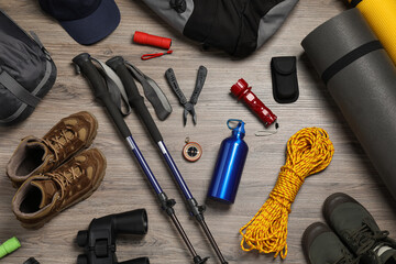 Flat lay composition with trekking poles and other hiking equipment on wooden background