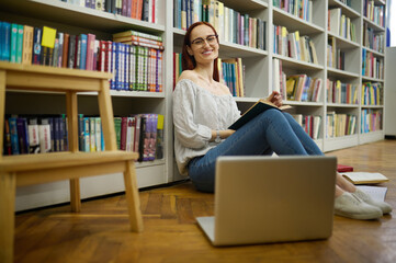 Woman with book sitting on floor near bookshelves