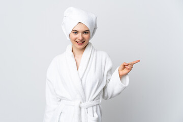 Teenager girl in a bathrobe isolated on white background surprised and pointing finger to the side