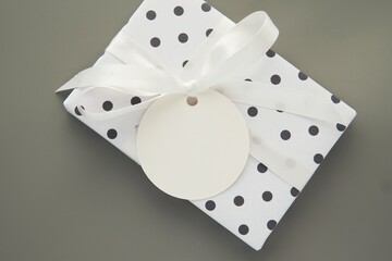 Round Christmas or Birthday gift label, tag mockup on package decorated with white ribbon and dotted wrapping paper.