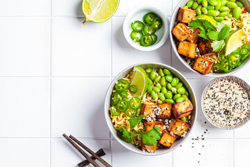 Vegan noodles ramen soup with marinated tofu, edamame beans and hot peppers in gray bowls.