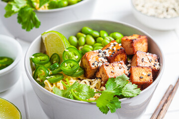 Vegan noodles ramen soup with marinated tofu, edamame beans and hot peppers in gray bowls.