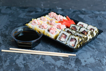 Delicious sushi with soy sauce, fish, cheese, caviar, wasabi and ginger in plastic packaging for takeaway on a dark background